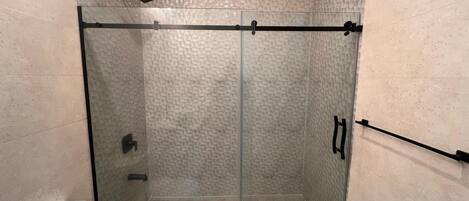 A glass-enclosed shower stall with a textured wall, a handheld showerhead, and a towel rack.