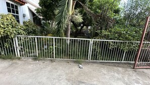 Un suelo de concreto con una cerca de metal blanco, rodeado de diversas plantas y árboles verdes.