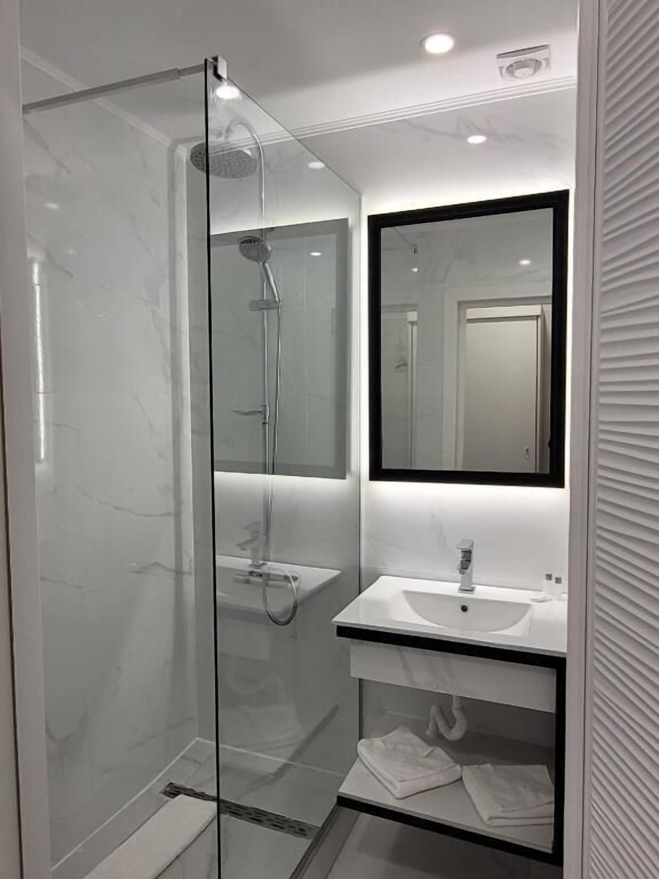 Une salle de bain moderne avec une douche à parois de verre, un lavabo blanc et un miroir au-dessus du lavabo.