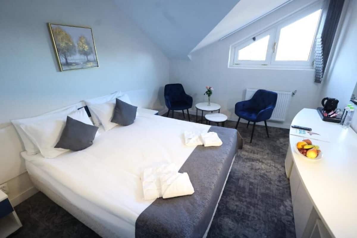 A hotel room with a bed, two chairs, a small table, and a desk with a fruit bowl.