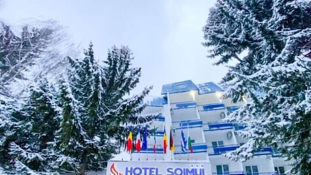 A hotel with a modern design, featuring a prominent entrance and multiple flags. - Hotel Soimul (Brasov)