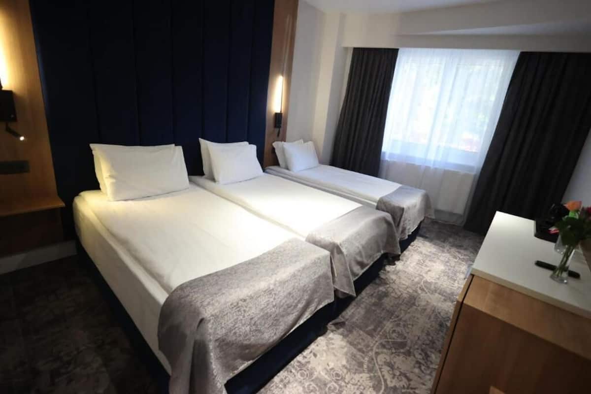 A hotel room with two beds, a desk, and a window with curtains.