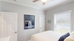 A bedroom with a bed, a ceiling fan, a window with blinds, and a framed picture on the wall.