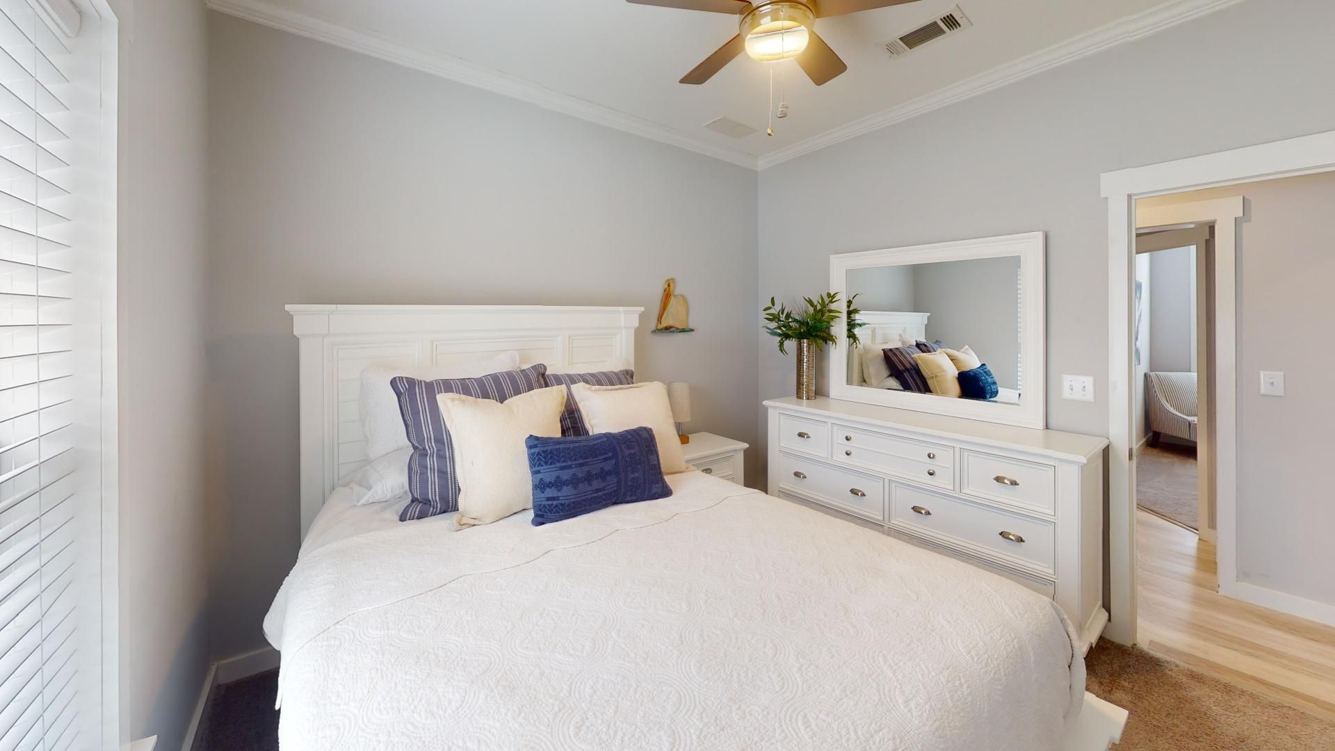A bedroom with a bed, dresser, mirror, ceiling fan, and a view into another room.