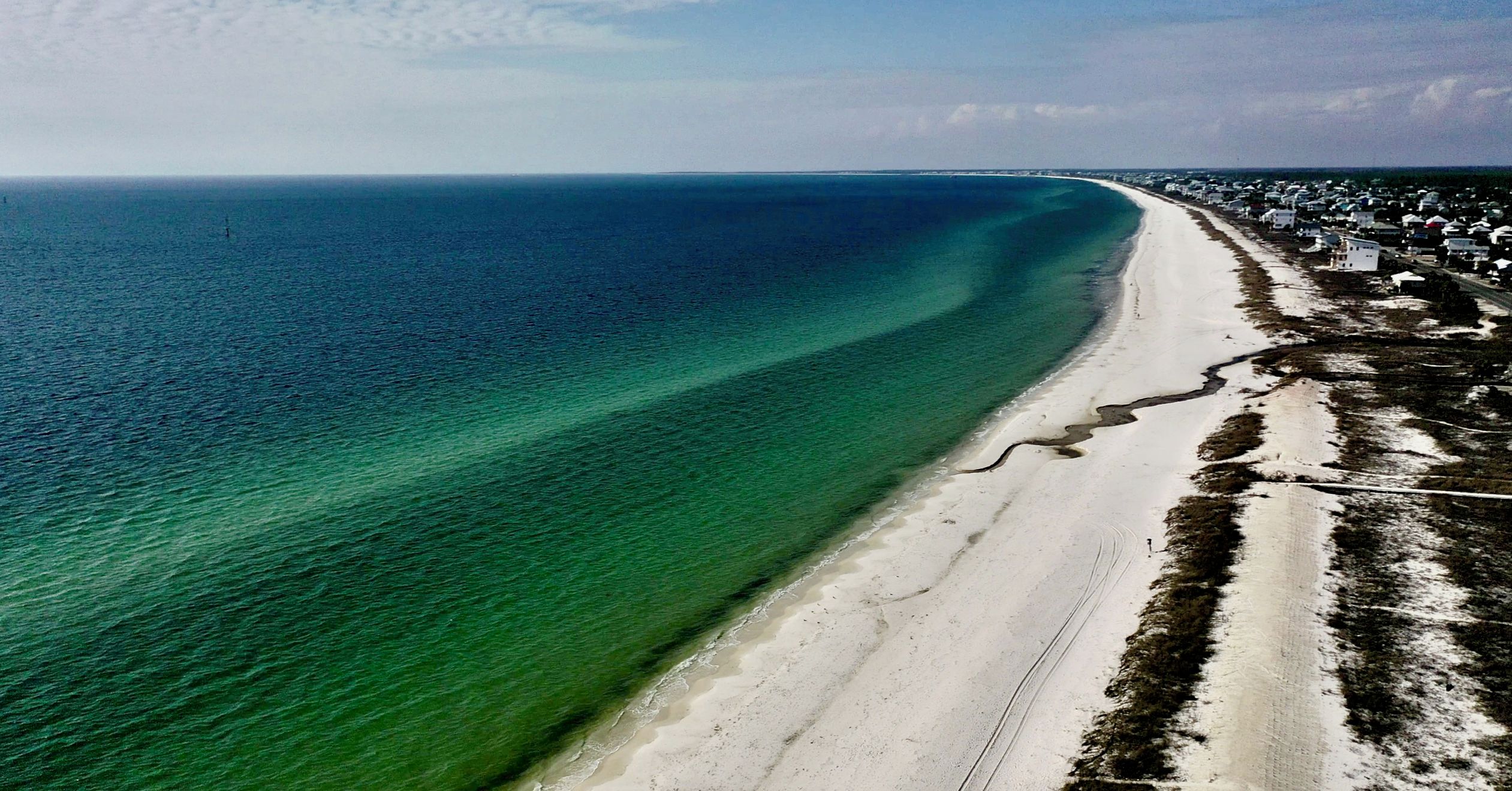 Une vue aérienne d’une plage où l’on distingue clairement la démarcation entre l’océan et le rivage sablonneux.