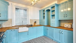 Une cuisine avec des meubles de couleur bleue, un plan de travail en bois, un évier et une fenêtre avec des stores.