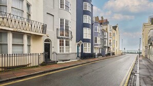 Une rangée de maisons mitoyennes aux façades blanches et bleu foncé, un ciel dégagé et une rue paisible.