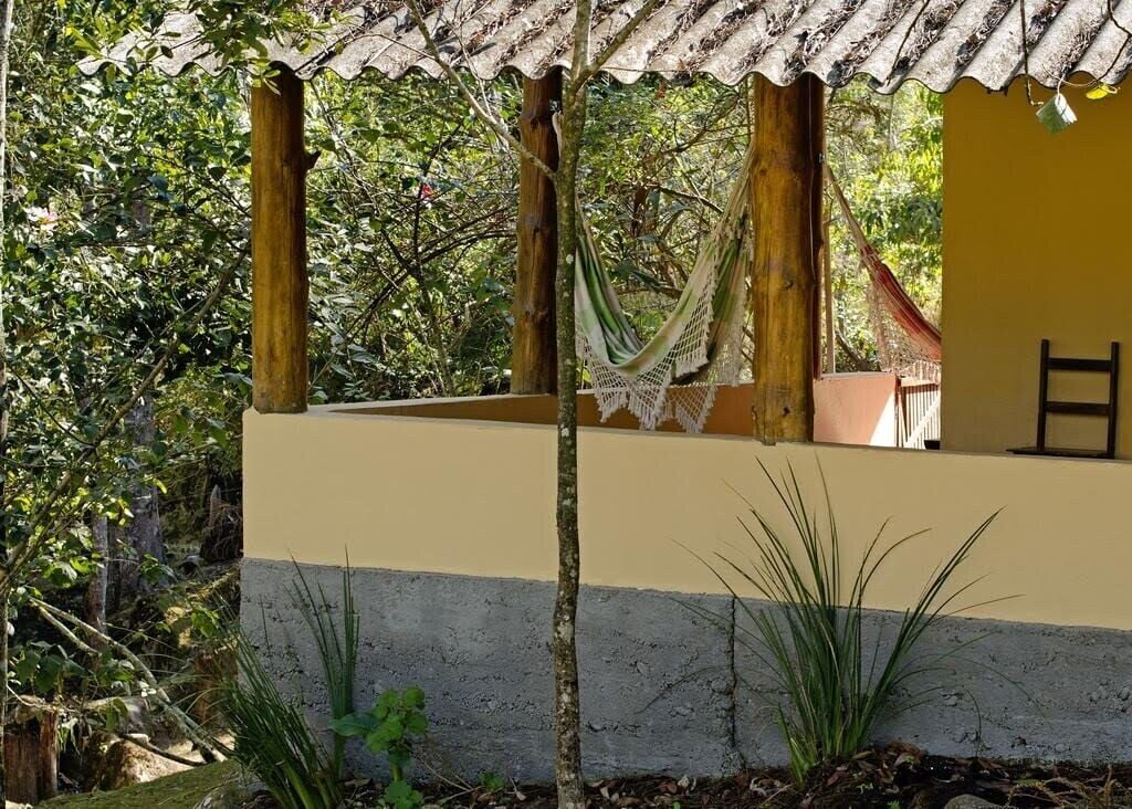A covered outdoor area with a hammock, wooden pillars, and a yellow wall.