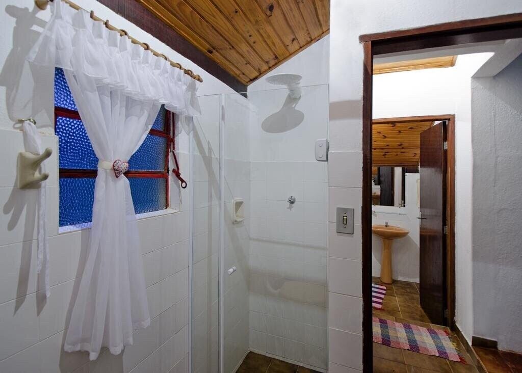 Un baño con paredes de azulejos blancos, techo de madera, zona de ducha y un lavabo sobre un pedestal de madera.