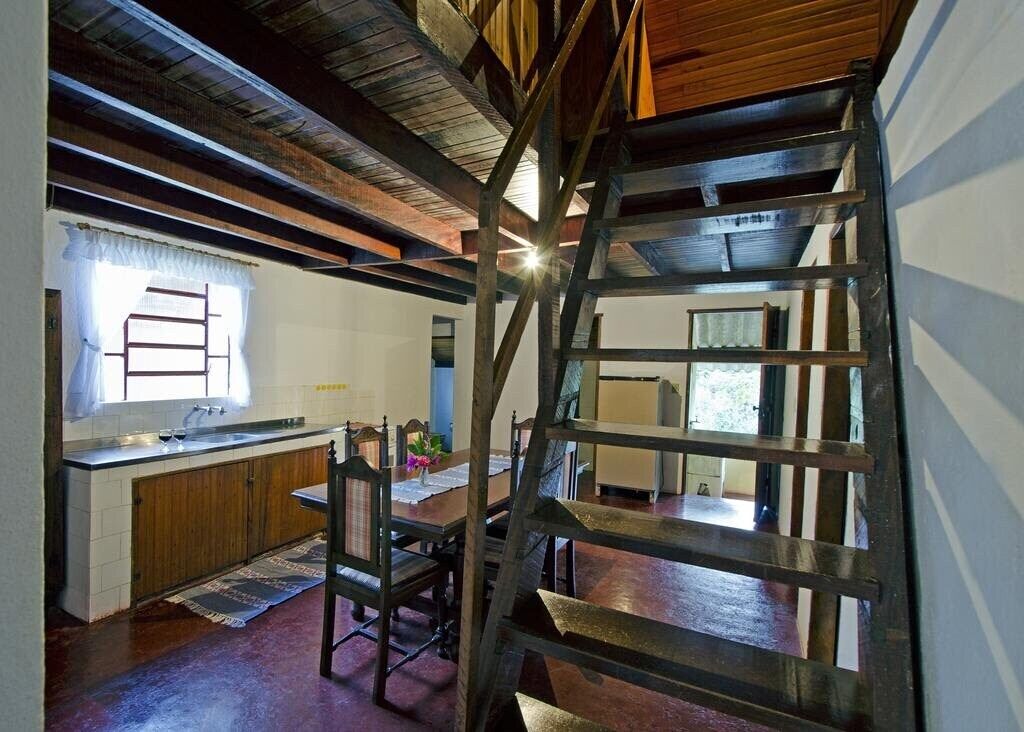 A kitchen with wooden beams, a window with curtains, a sink, and a dining area with a chair and table.