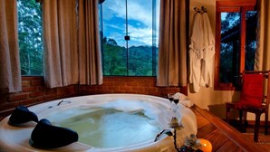 A hot tub in a room with a view of the forest, wooden flooring, and a chair with a red towel. - Pousada da Gruta  (Maromba)
