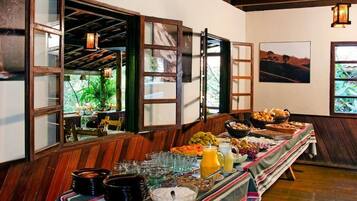 A buffet table with various food items and drinks, wooden walls, and a view of greenery outside.