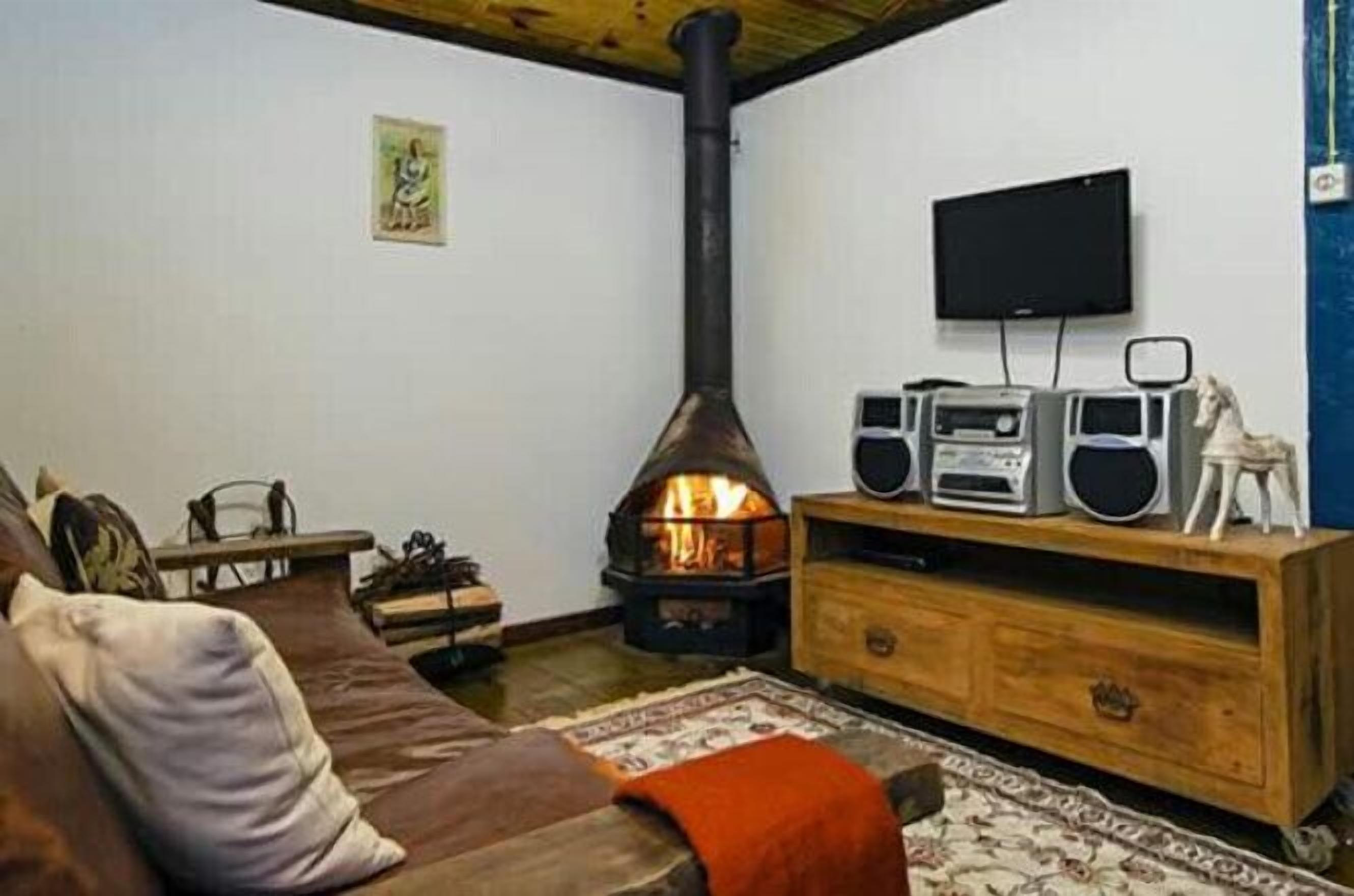 A cozy living room with a wood-burning stove, a television mounted on the wall, and a wooden cabinet with speakers.