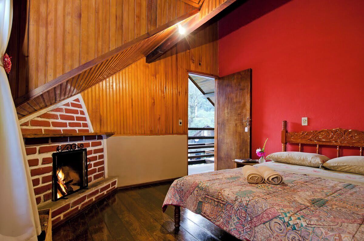 Een kamer met een haard van baksteen, een bed met een bedovertrek met dessin, en een rode wand.