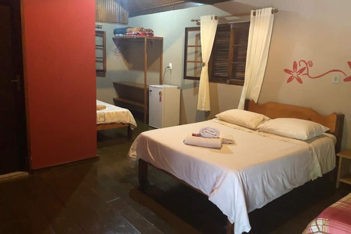 A bedroom with a bed, a small table, a wardrobe, and a window with curtains.