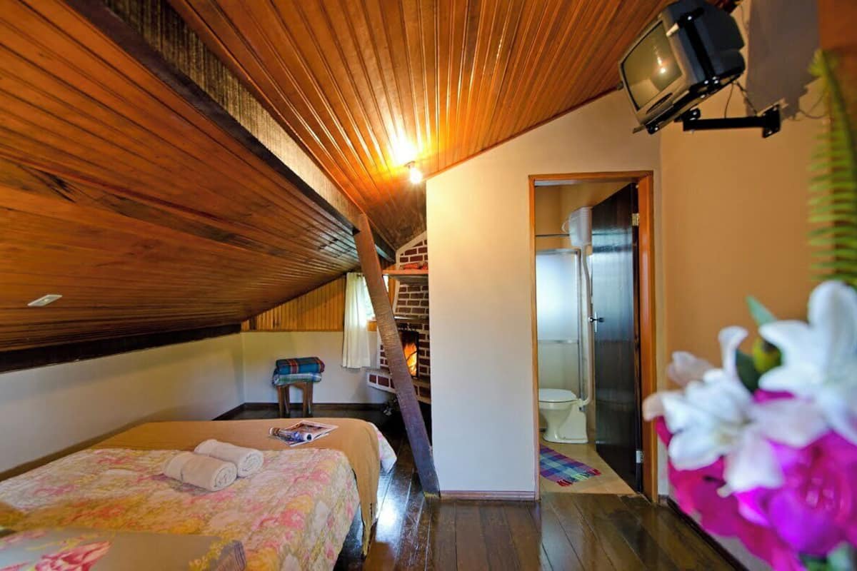 A cozy attic bedroom with wooden beams, a bed with floral bedding, a small table, and a television.
