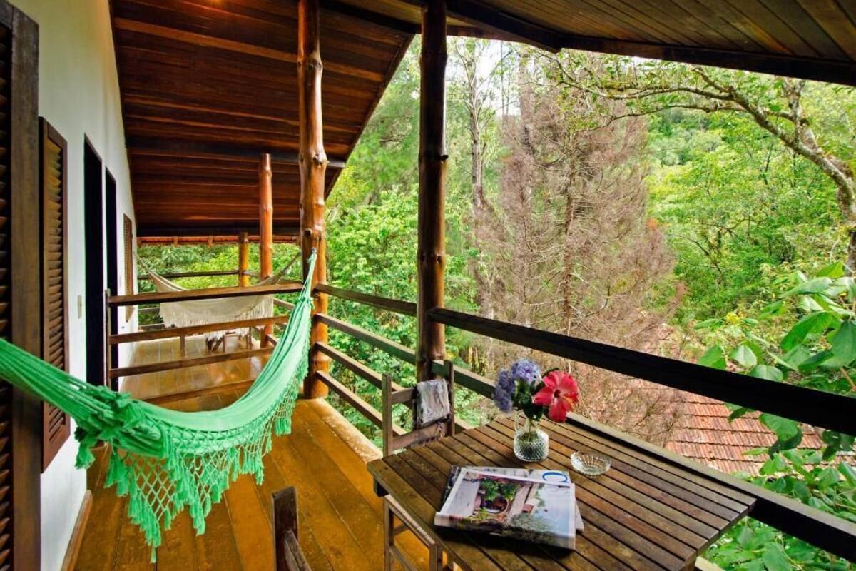 A wooden deck with a hammock, a table with a vase of flowers, and a view of lush greenery.