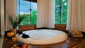 A hot tub in a room with large windows, a brick wall, and a wooden floor. - Pousada da Gruta  (Maromba)