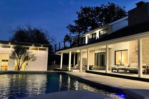 A modern two-story house with a swimming pool, outdoor seating, and a stone facade.