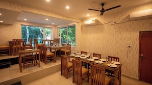 A dining area with wooden furniture, large windows, and an air conditioning unit. - Hotel Marine (Varanasi)