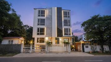 A multi-story building with a modern design, featuring a central vertical glass facade and a gated entrance.