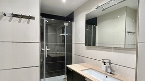 A modern bathroom with a large mirror, a sink, and a shower area.