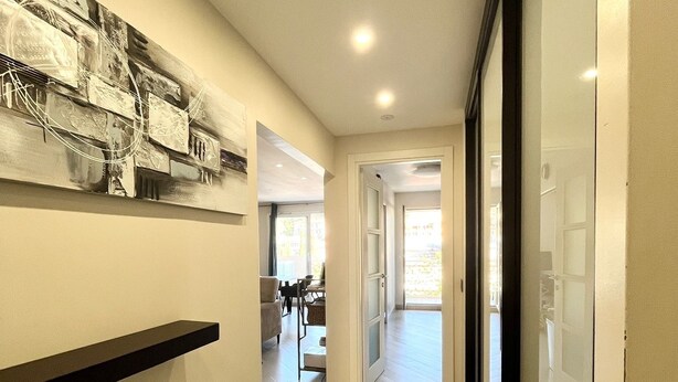 A hallway with a black shelf, a ceiling with recessed lighting, and a door leading to a room with a view.