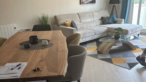 A modern living room with a wooden dining table, grey sofa, and a glass coffee table.