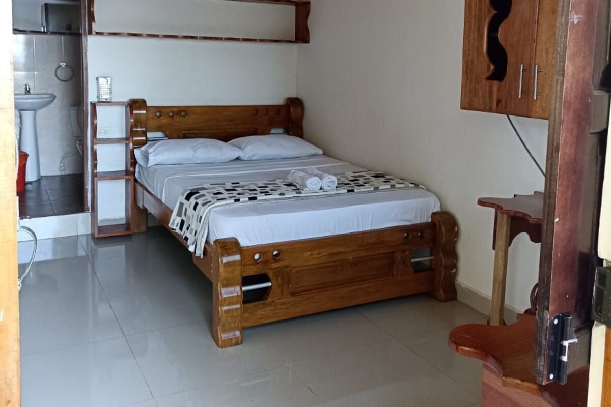 A bedroom with a wooden bed, a small bedside table, a wall-mounted air conditioner, and a wooden cabinet.