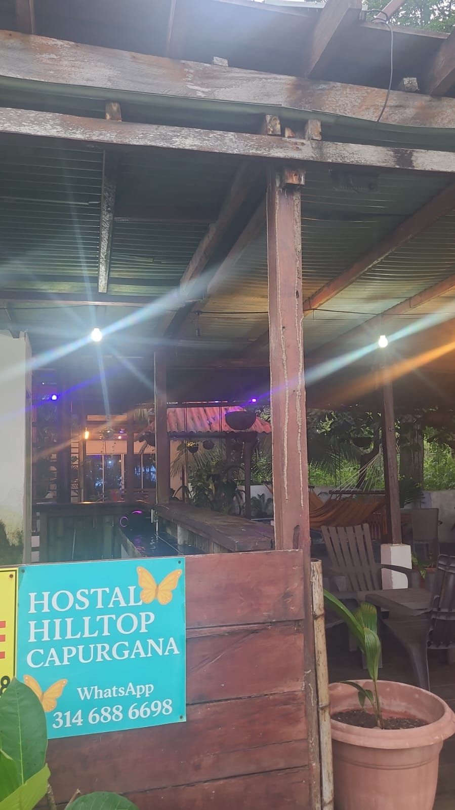 Una estructura rústica de madera con un cartel que indica Hostal Hilltop Capurgana, e incluye un número de contacto de WhatsApp.