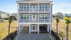 Ein zweistöckiges Strandhaus mit einem Balkon im oberen Stockwerk, einer überdachten Veranda und Blick auf den Strand.