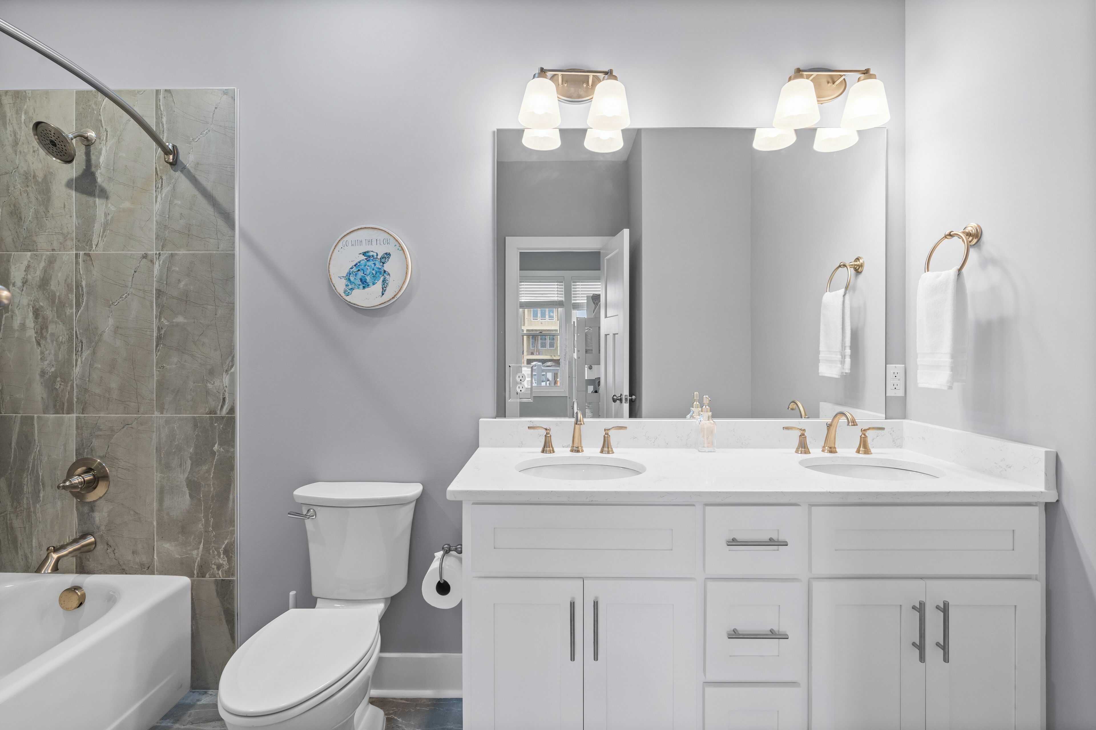 A modern bathroom with a double sink vanity, a bathtub, and a toilet.