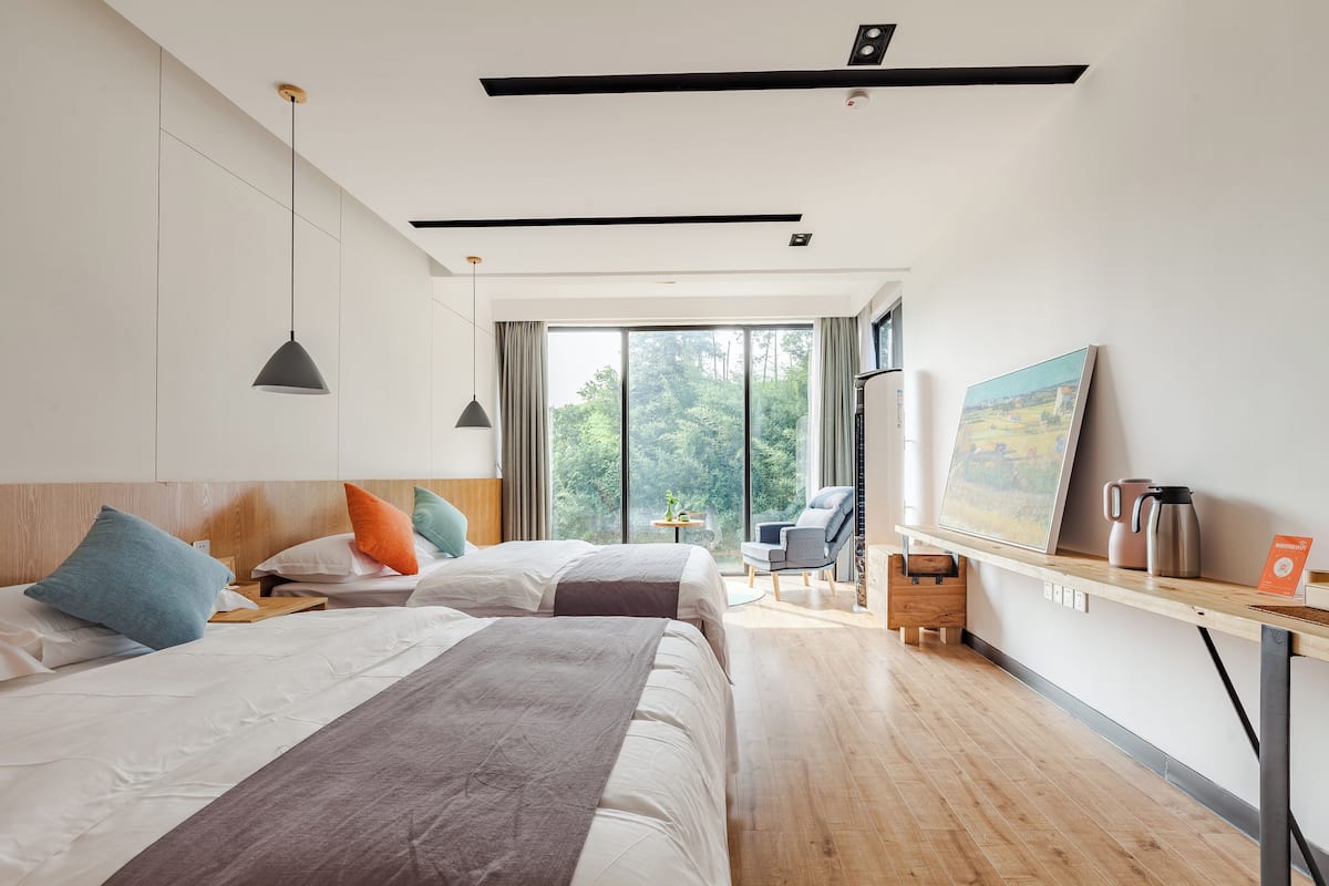 Ein modernes Hotelzimmer mit zwei Betten, einem Schreibtisch, einem Sessel, einer Kaffeemaschine und einem Bild an der Wand.