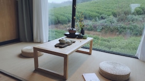 A room with tatami flooring, a low wooden table with tea utensils, and a view of a green field through a large window. - YOUTEA Holiday Villa (Huzhou)