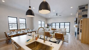A modern kitchen with a central island, dining area, and living space with large windows.