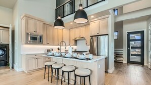A modern kitchen with a central island, bar stools, stainless steel appliances, and pendant lighting.