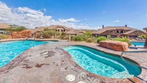 Ein Poolbereich mit mehreren Pools, einer Betonplattform und einer Reihe von Häusern im Hintergrund.