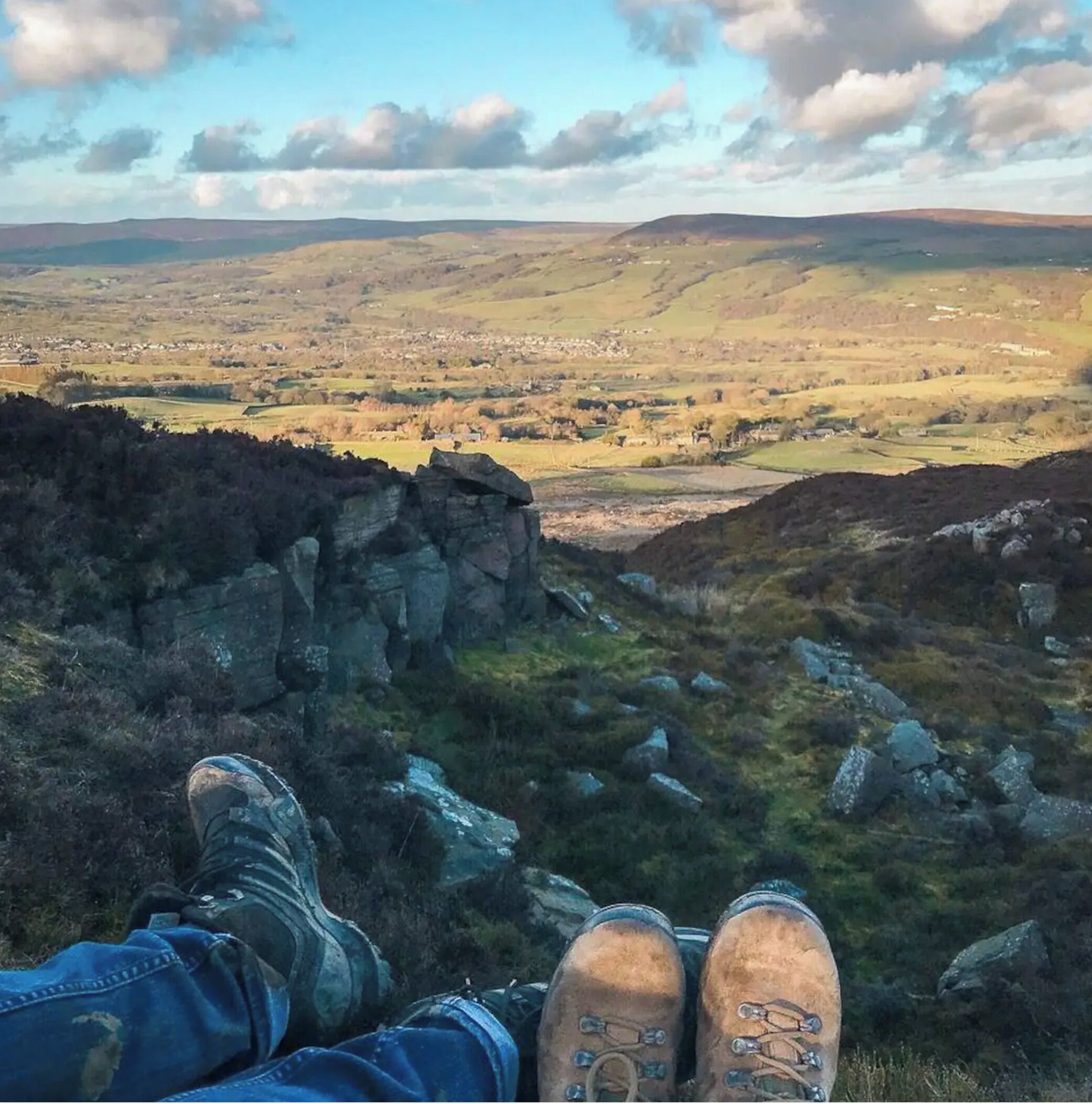 A person sitting on a rocky outcrop overlooking a valley with scattered buildings.