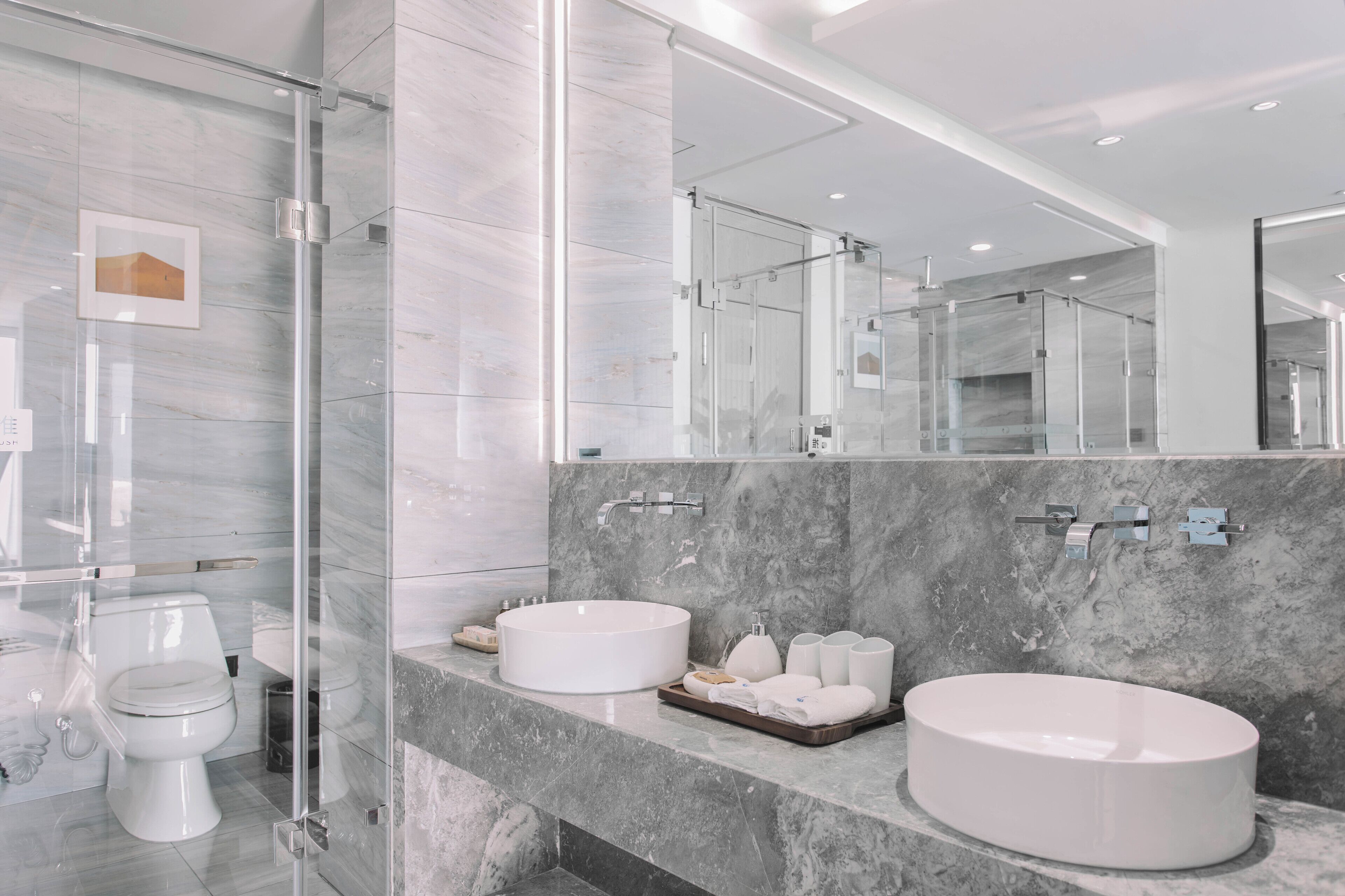 A modern bathroom with a glass shower enclosure, a toilet, and two sinks with marble countertops.