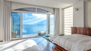 A bedroom with a large sliding glass door leading to a balcony with a view of the sea.