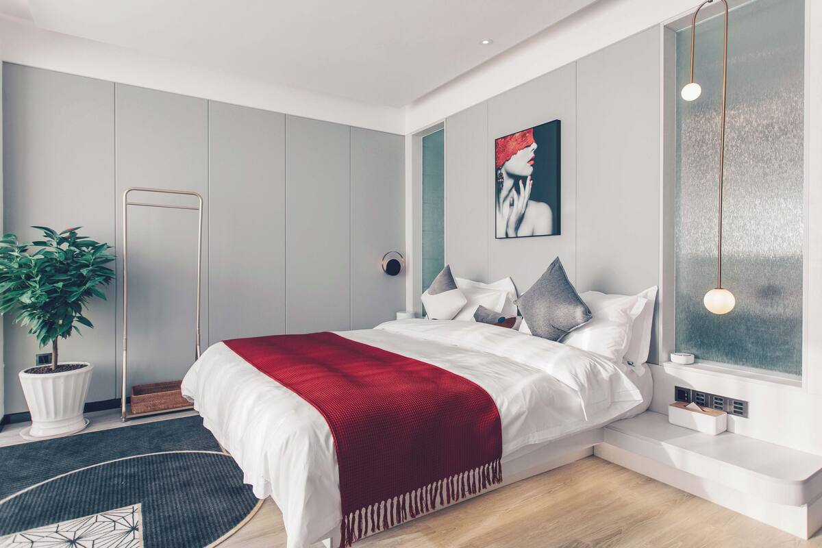 Une chambre à coucher moderne avec un lit, une plante en pot, une lampe sur pied et une fenêtre donnant sur un beau paysage.