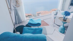 A modern room with a view of the sea, a blue sofa, a small table with a vase, and a chair.