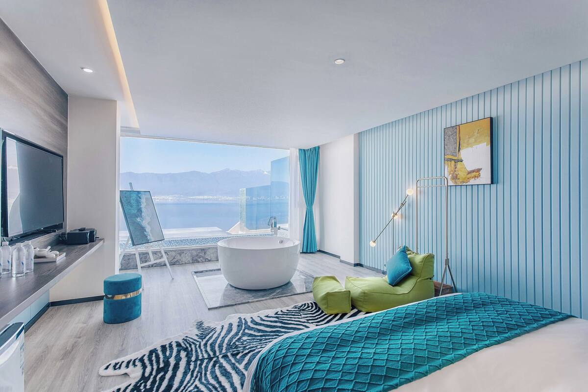 Une chambre d’hôtel moderne avec un grand lit, une baignoire, une télévision et une vue sur l’océan.