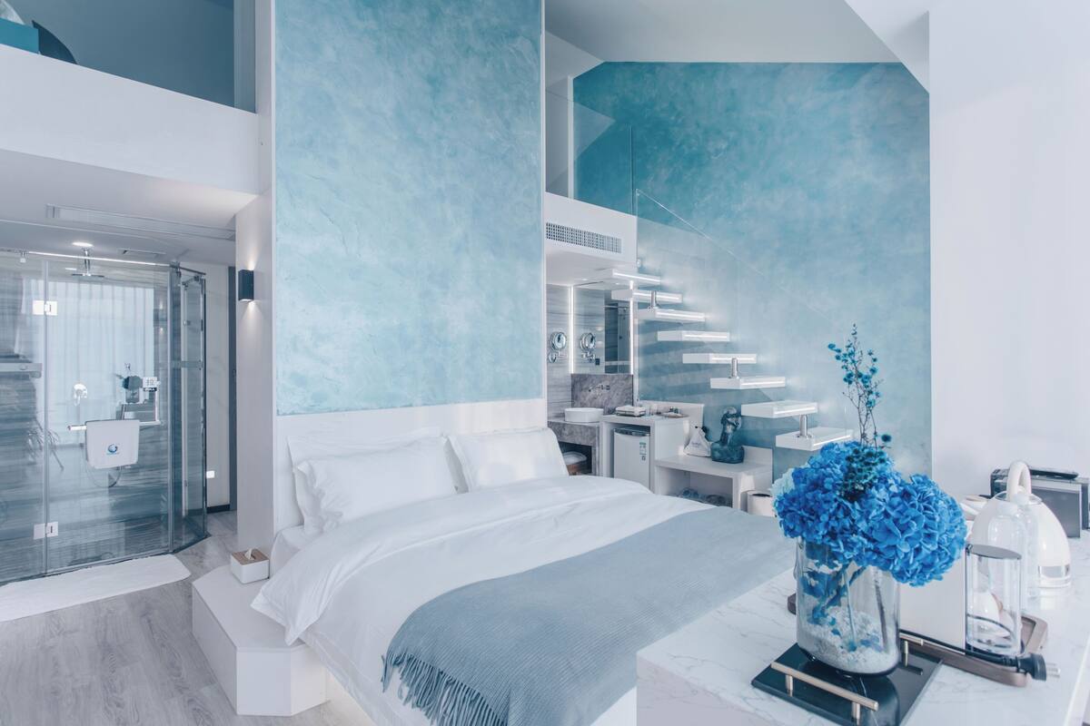 Une chambre à coucher moderne avec un grand lit, une douche en verre et une vue sur la cuisine et l’espace de vie.