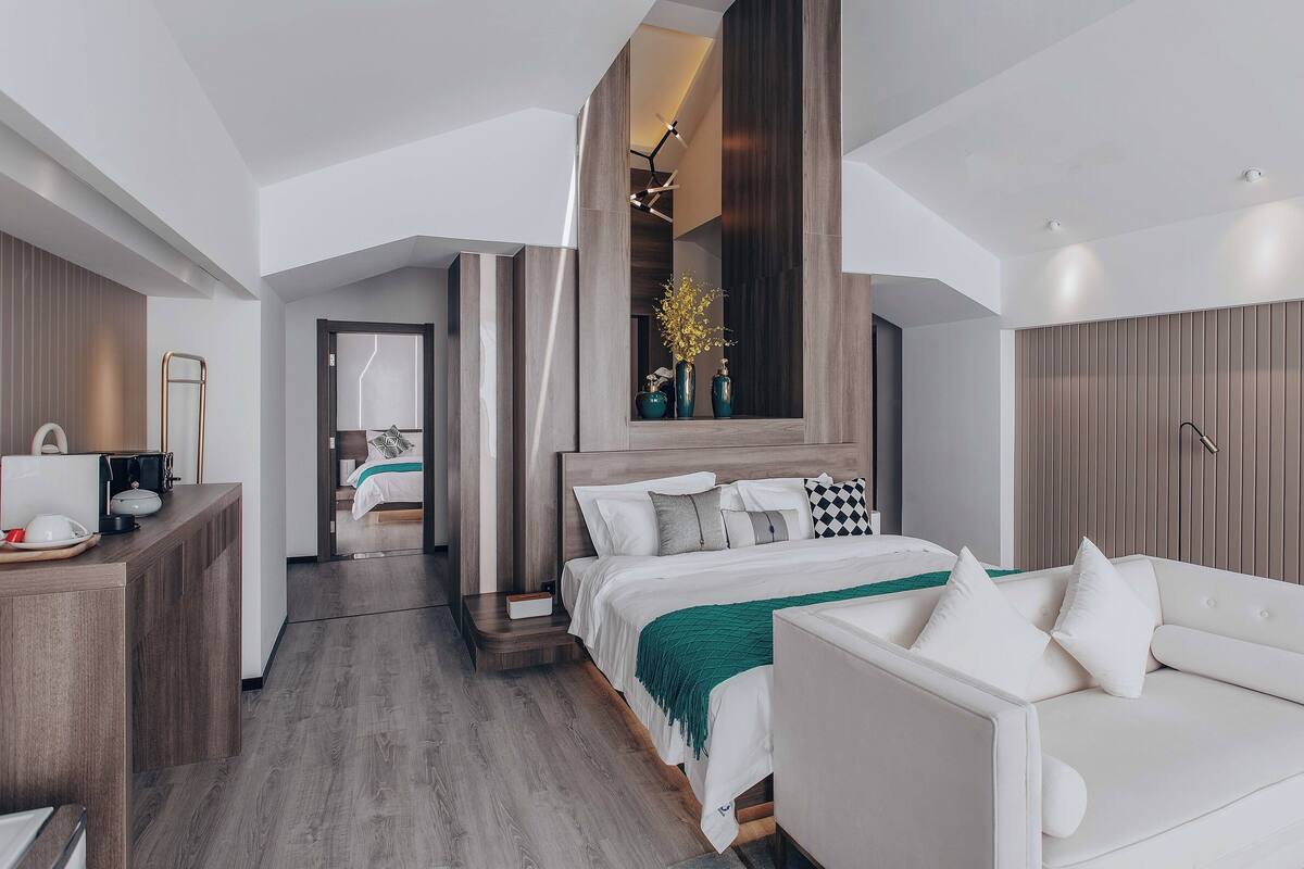 Une chambre d’hôtel moderne avec un lit, un canapé blanc, un bureau avec un ordinateur et un miroir.