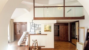 A spacious loft with a high ceiling, a wooden staircase, a kitchen area, and a dining space.