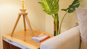 A wooden bedside table with a lamp, a book, and a large green plant. - Acropolis Central Living (Athina)