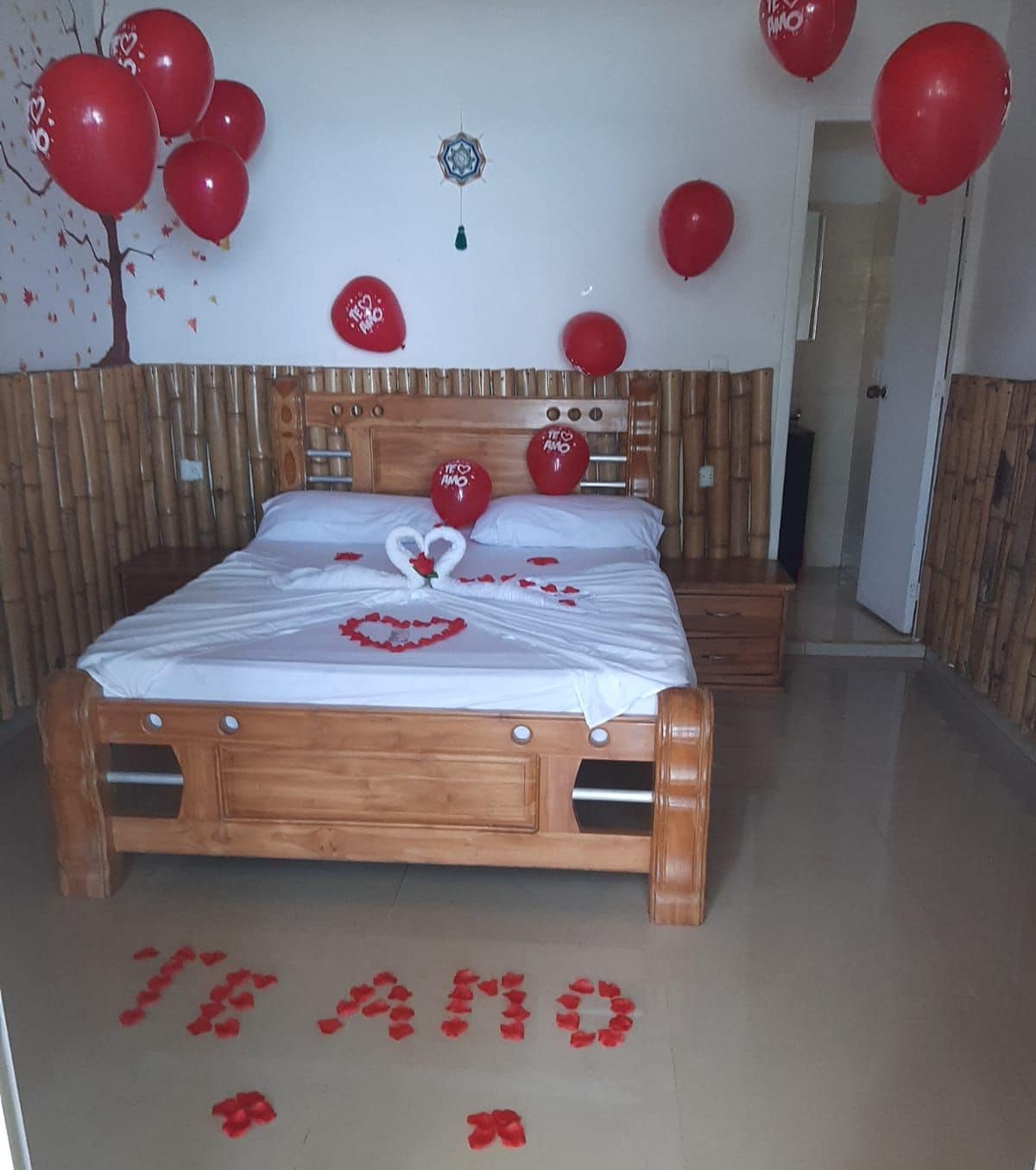 Un dormitorio con una cama de madera, globos rojos y una decoración con forma de corazón sobre la cama.