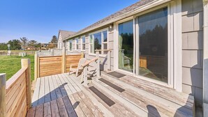 A wooden deck with outdoor seating, large sliding glass doors, and a view of the surrounding area.