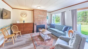 A cozy living room with a brick fireplace, a sofa, a coffee table, and a view of the outdoors.